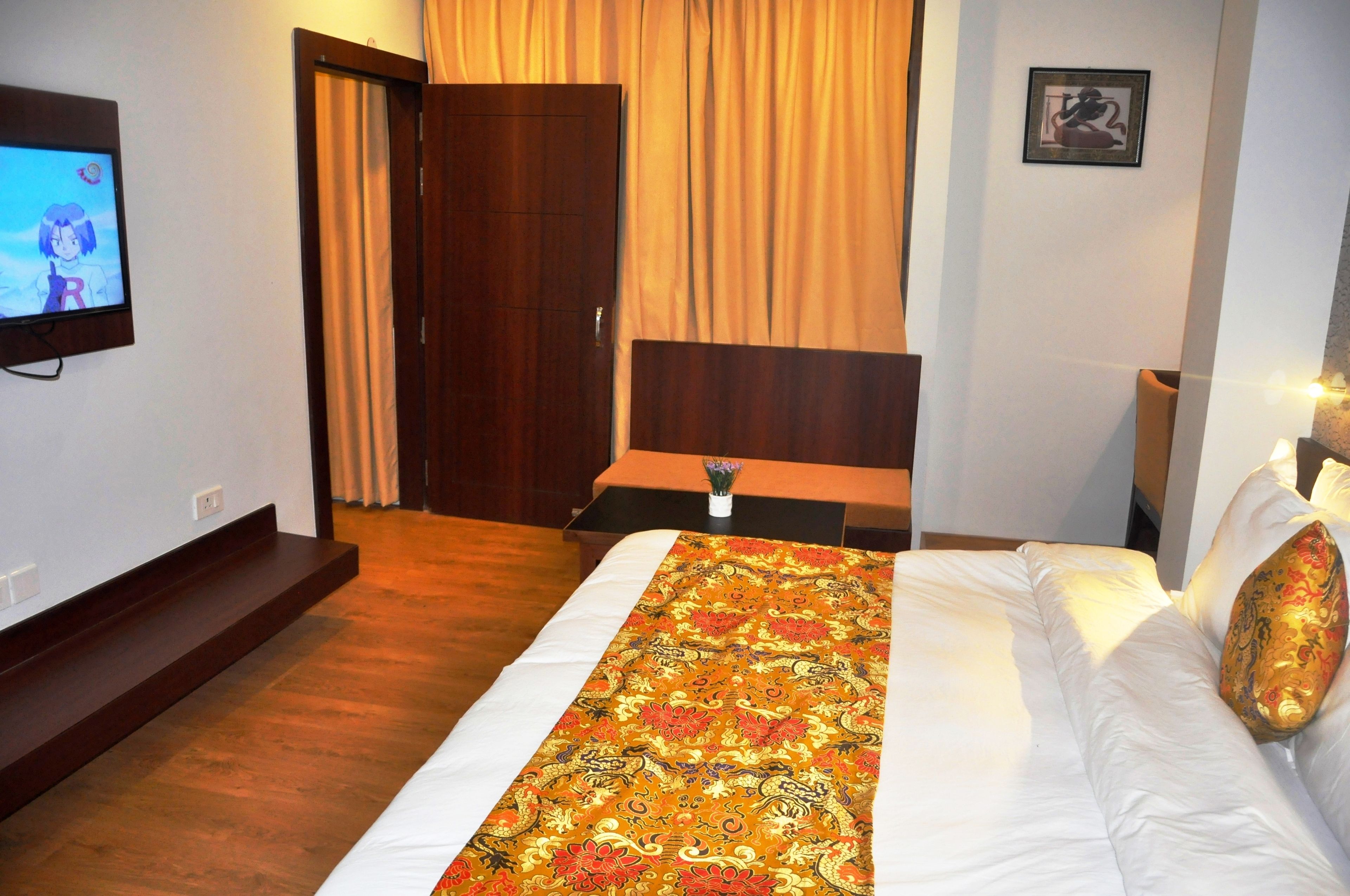A hotel room with a bed, a TV, a wooden headboard, a curtain, and a framed picture on the wall.
