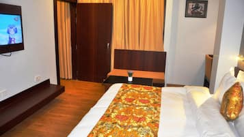 Una habitación de hotel con cama, televisión, cabecera de madera, cortina y un cuadro enmarcado en la pared.