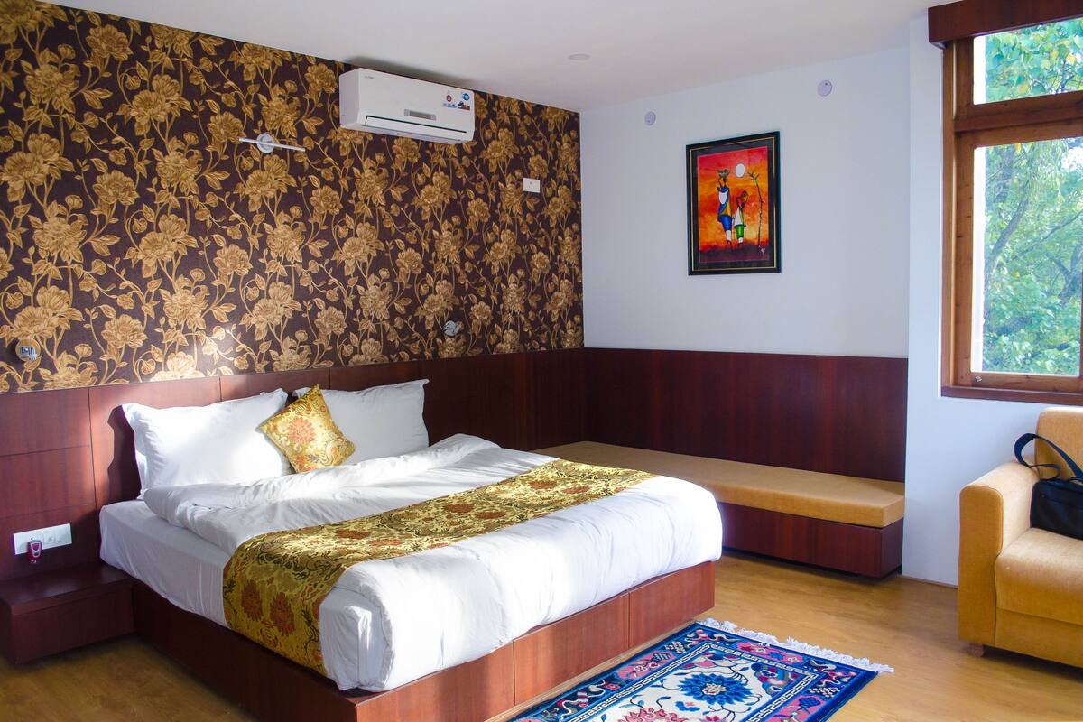 A hotel room with a large bed, a bench, a window with a view of trees, and a floral-patterned wall.