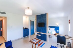 Una habitación de hotel moderna con una televisión de pantalla plana, un escritorio con una silla, una mesita con un periódico y una pared azul decorativa.