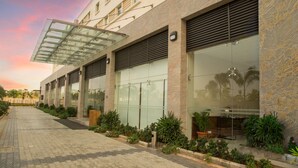 A modern building with large glass windows, a covered walkway, and a landscaped garden area.
