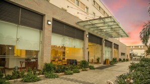 A modern hotel with a glass facade, outdoor seating, and a landscaped garden area.