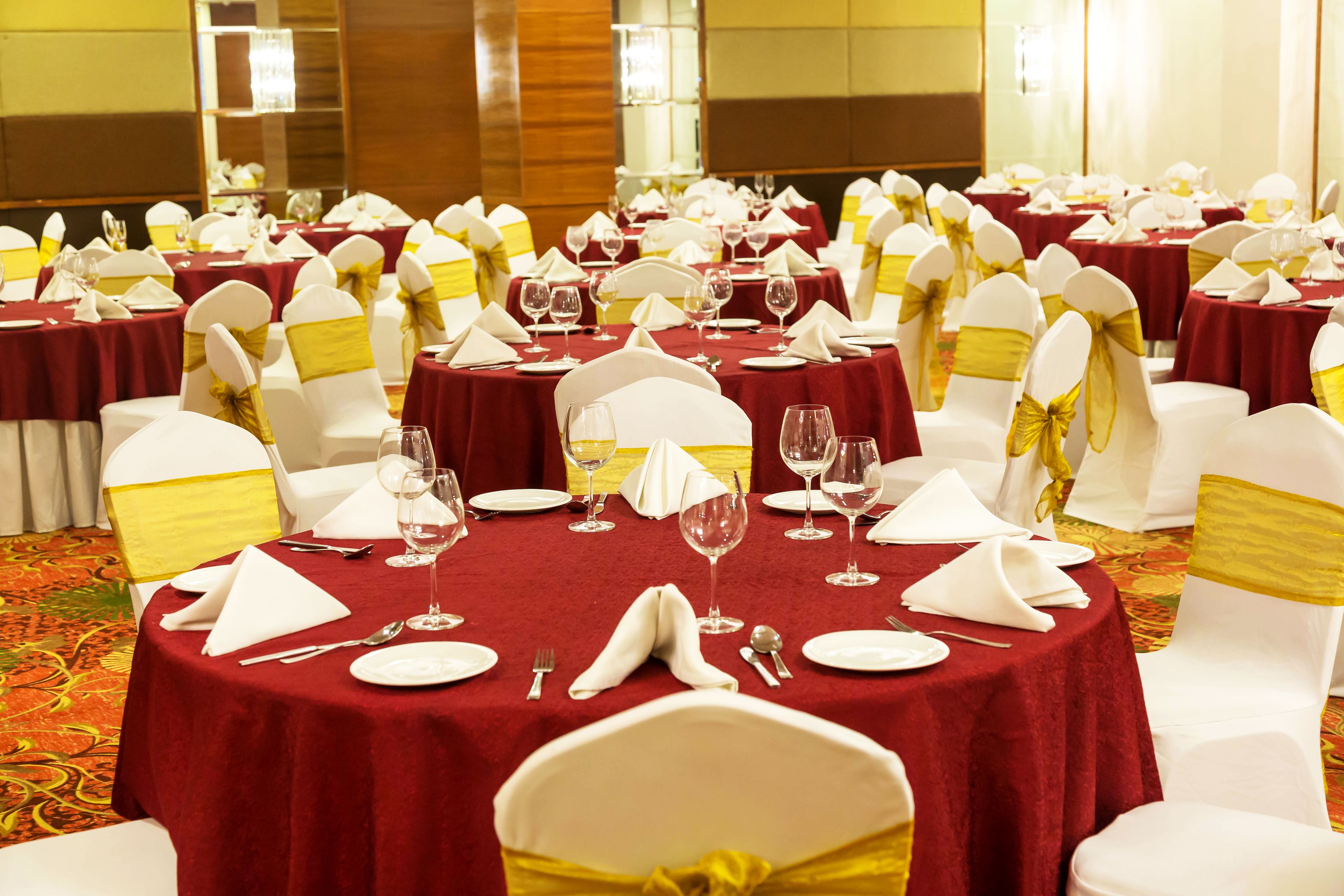 A banquet hall with round tables covered in red tablecloths, white chairs with yellow sashes, and neatly arranged dining ware.