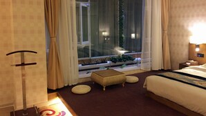 Une chambre d’hôtel comprenant un lit, un petit coin salon, une fenêtre avec des rideaux, une table de chevet et une lampe.