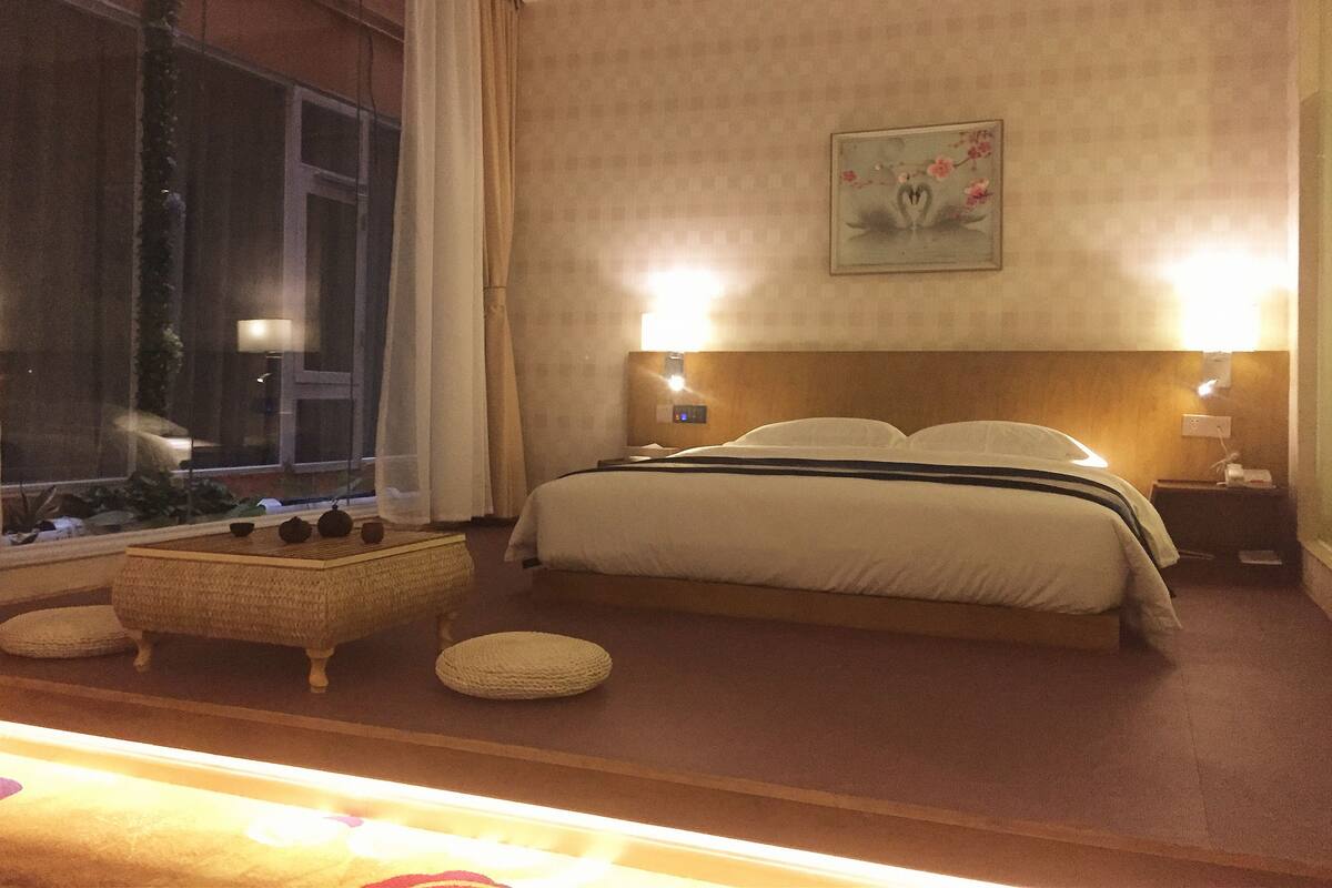 A neatly arranged hotel room with a large bed, bedside lamps, a small table with decorative items, and a window with curtains.