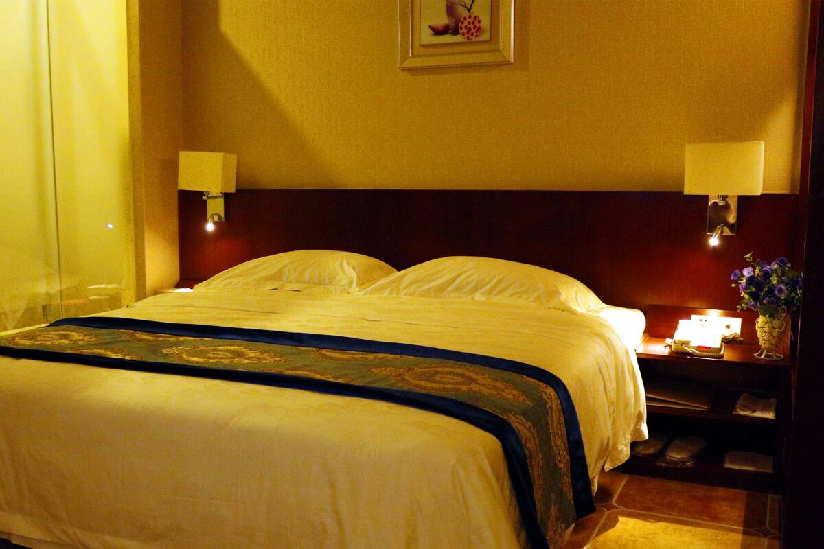 A hotel room with a large bed, two bedside lamps, a nightstand with a phone, and a framed picture on the wall.