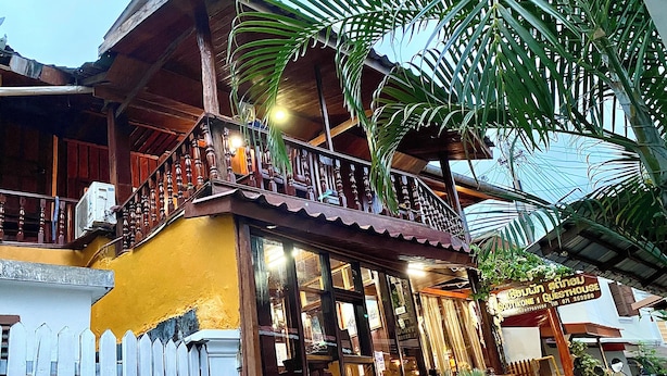 A traditional wooden building with a balcony, a white picket fence, and parked motorcycles. - Soutikone 1 Guesthouse (Luang Prabang)