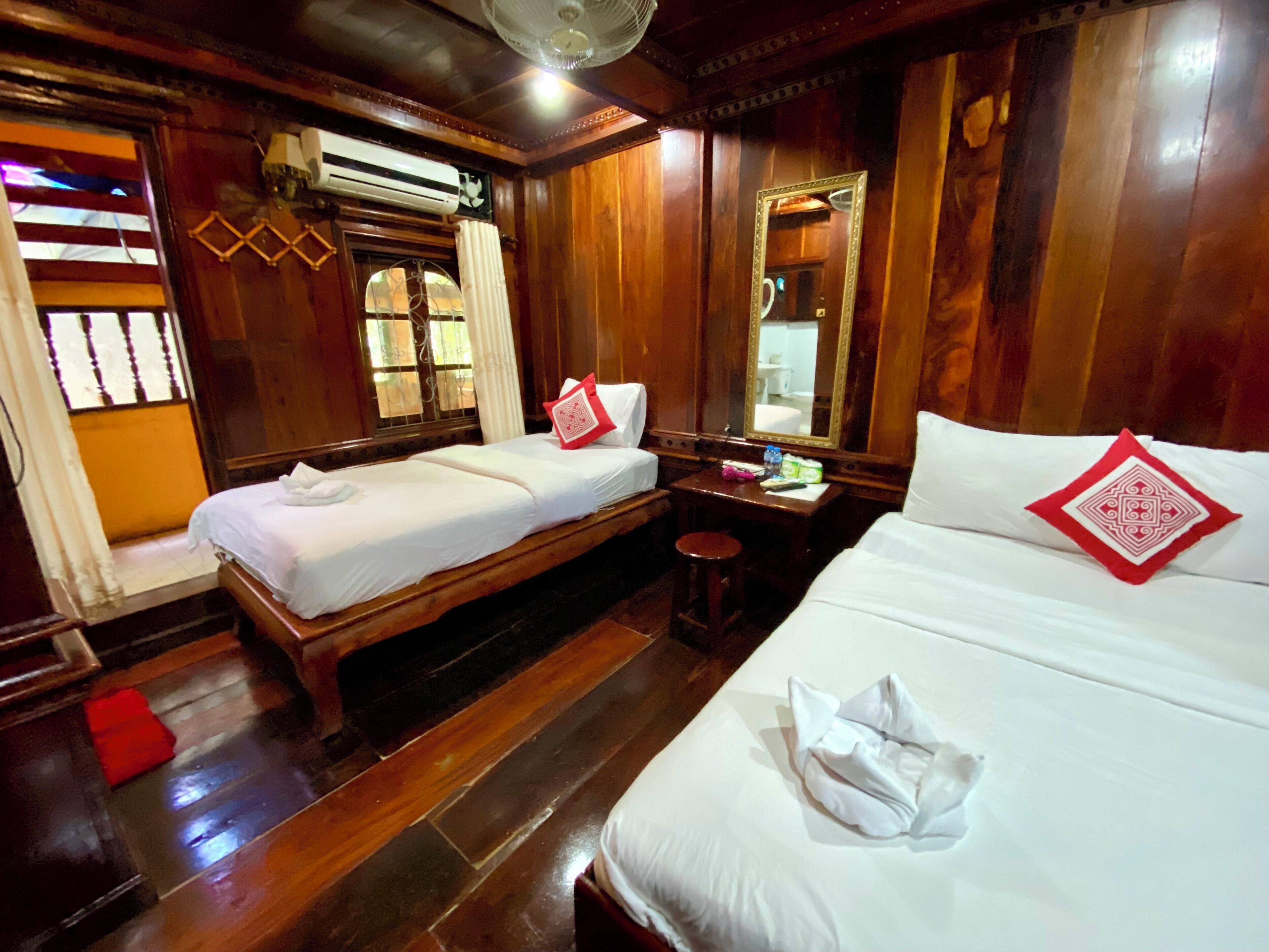 A hotel room with two wooden beds, a wooden desk, a mirror, and an air conditioning unit.