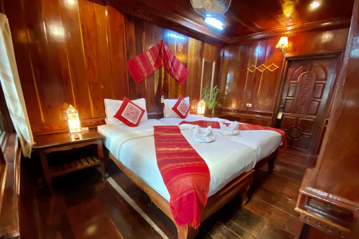 Une pièce en bois avec deux lits, chacun agrémenté de draps blancs et de touches de rouge, une table de chevet avec une lampe et une porte en bois.