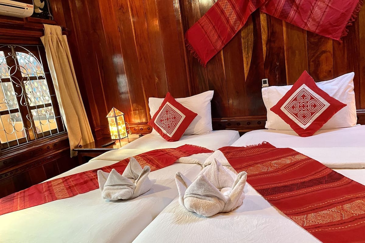 Une chambre d’hôtel avec deux lits, chacun recouvert d’une couvre-lit à motifs rouges et blancs, agrémentée d’oreillers blancs à motifs losangés rouges et d’un plaid rouge.