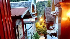 A narrow alleyway with buildings on either side, a wooden table with a chair, and a small table lamp. - Soutikone 1 Guesthouse (Luang Prabang)