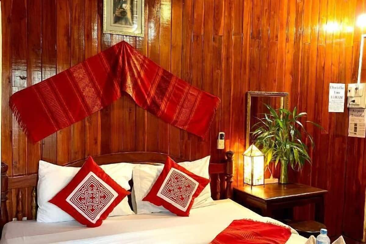 Une pièce aux murs lambrissés, avec un lit, des oreillers, une table de chevet, une plante et une bouteille d’eau.