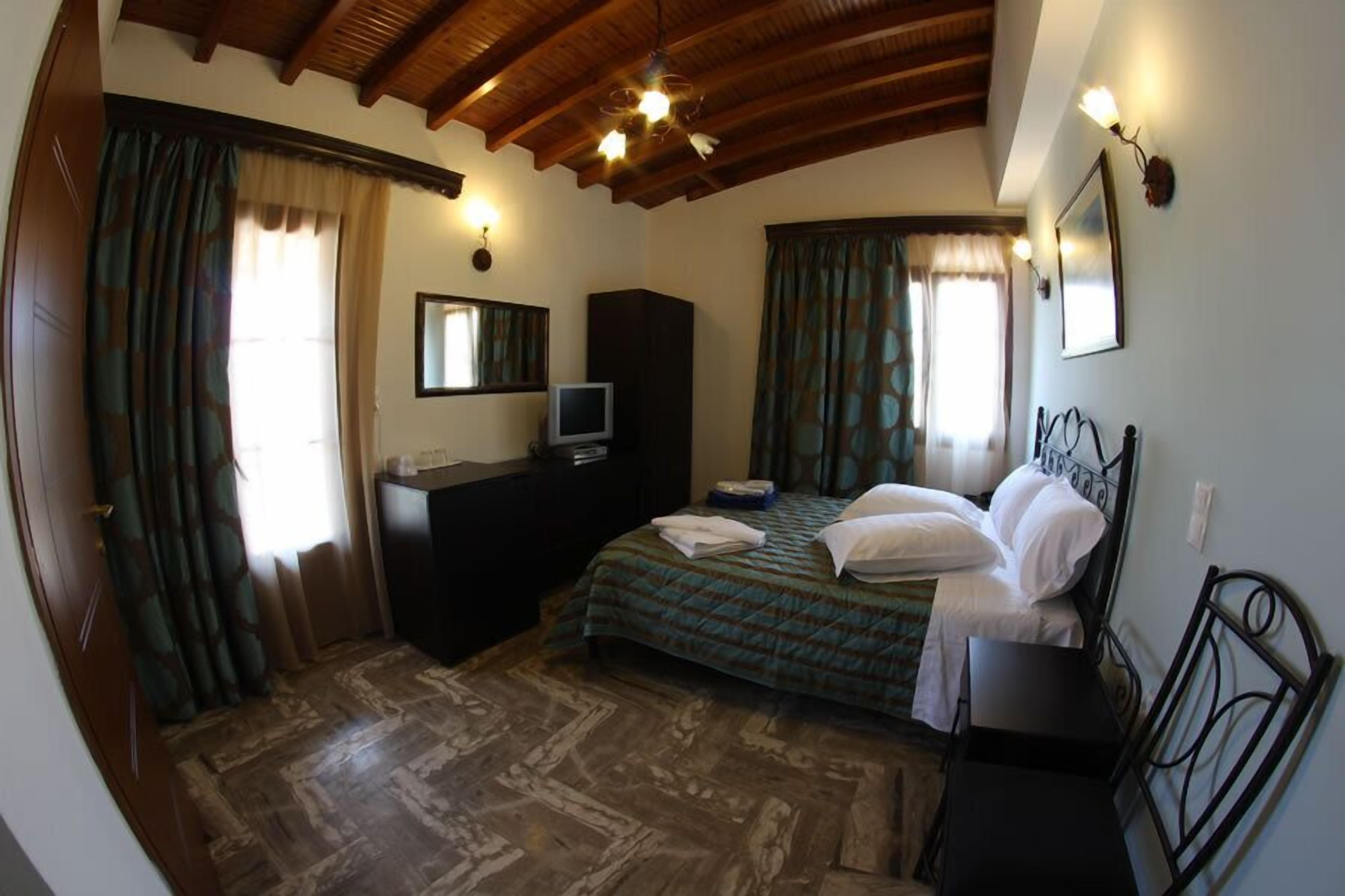 A bedroom with a wooden ceiling, a bed with white linens, a dresser, a television, and patterned curtains.