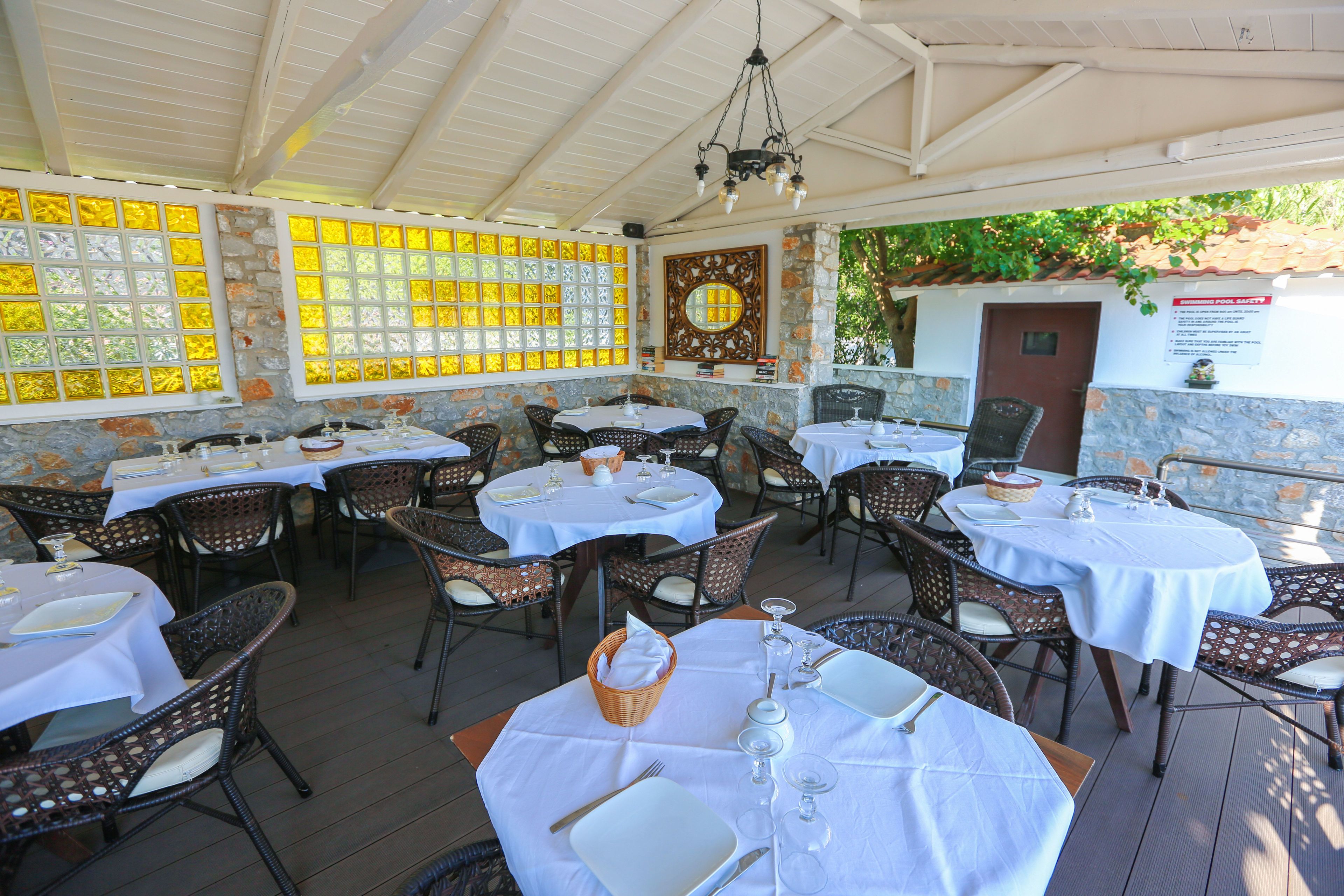 An outdoor restaurant with round tables, wicker chairs, and a stone wall.