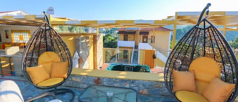 Terraza en la azotea con sillas de mimbre y una mesa, con vistas a una zona residencial.