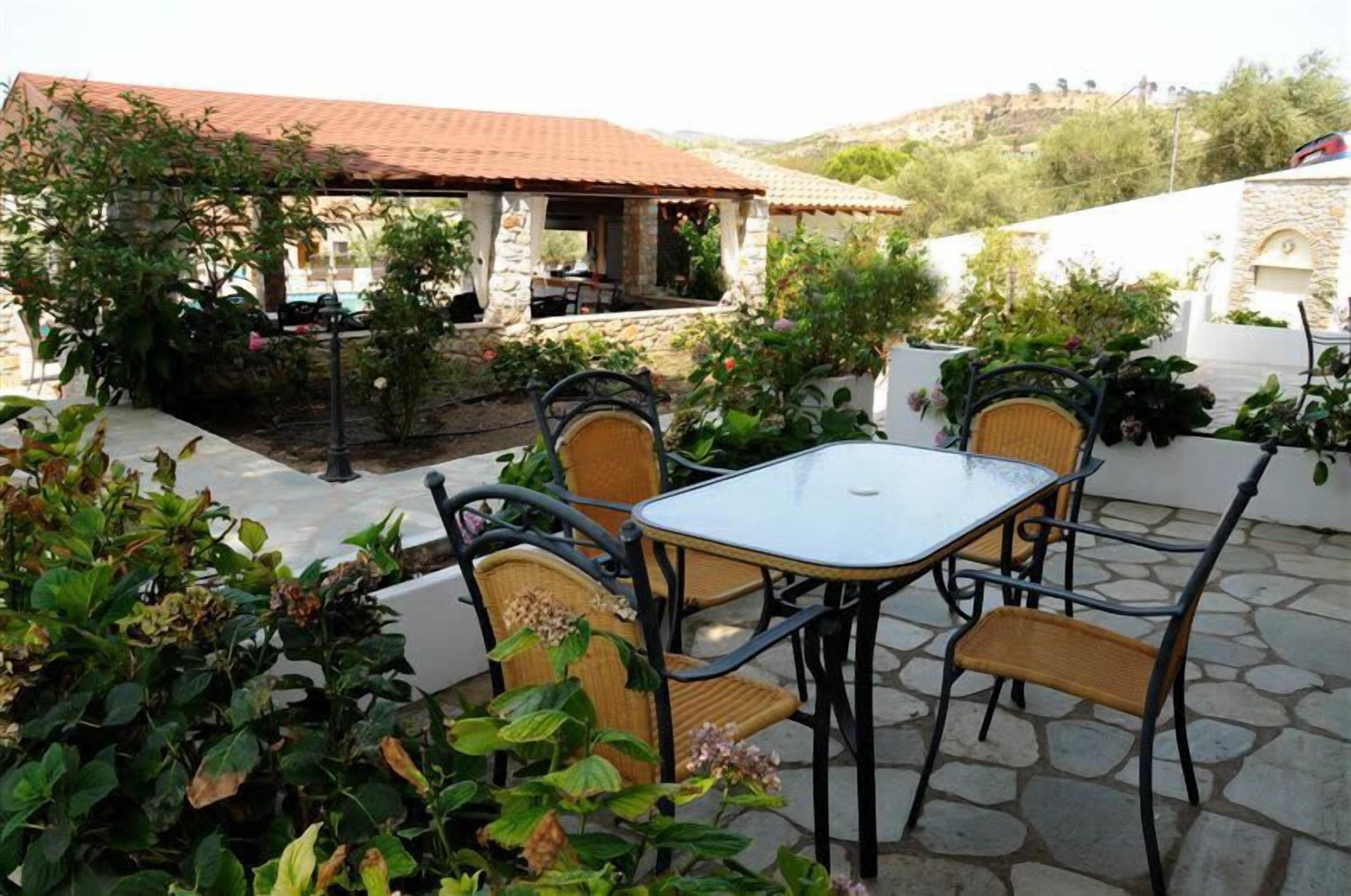 A patio with a table and chairs, surrounded by plants and a stone wall.