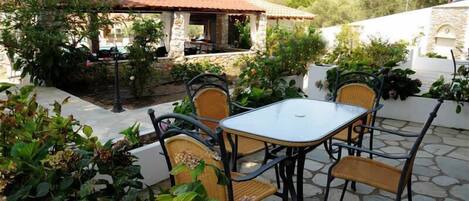 A patio with a table and chairs, surrounded by plants and a stone wall.