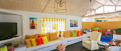 Un salón espacioso con un televisor grande, cojines coloridos, un sofá y una mesa con un jarrón de flores.