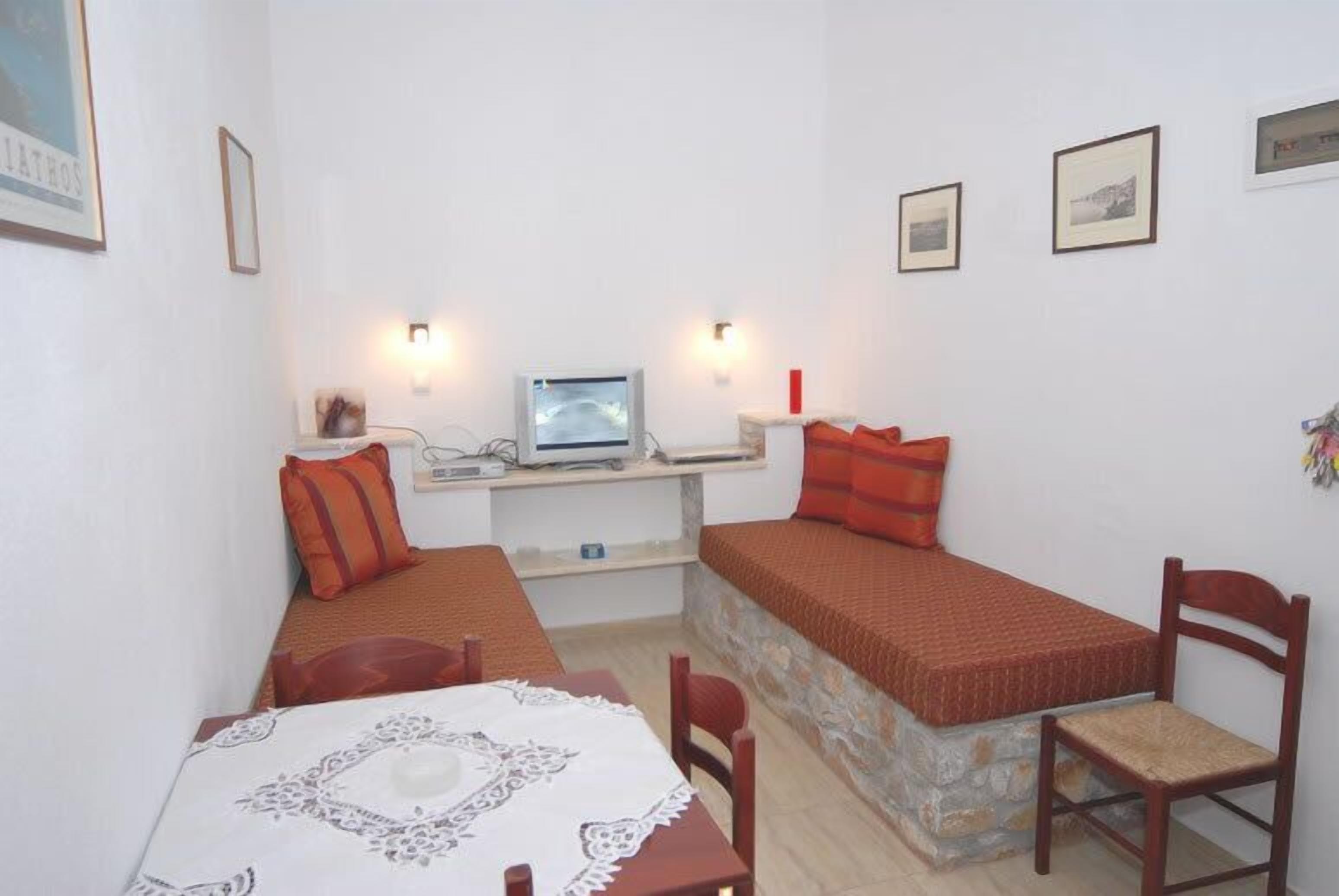 Une chambre de taille modeste, équipée de deux lits simples, d’une petite table recouverte d’une nappe en dentelle, d’une chaise, d’un bureau avec un ordinateur et d’un téléviseur.