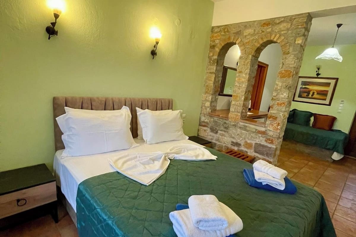 Un lit bien fait, avec du linge de lit et des serviettes blancs, une couvre-lit verte et une table de chevet dotée d’un tiroir.