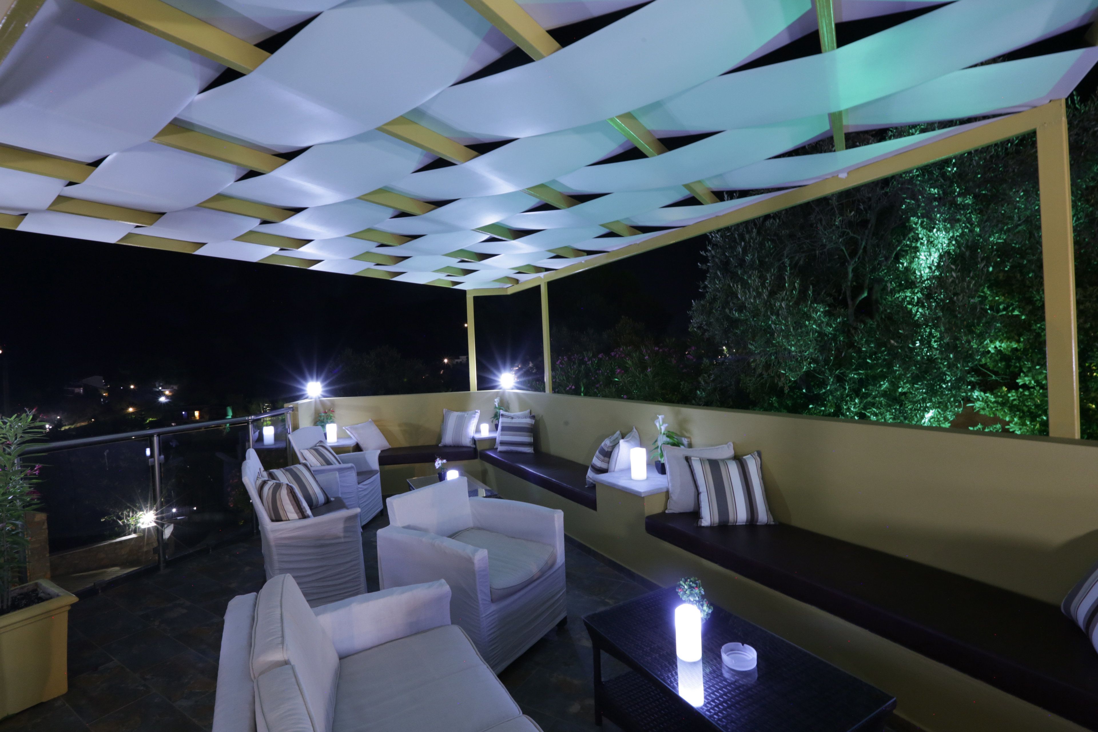 Un espacio de asientos al aire libre con sillas blancas acolchadas y una mesa oscura, bajo un techo con estampado blanco y amarillo.