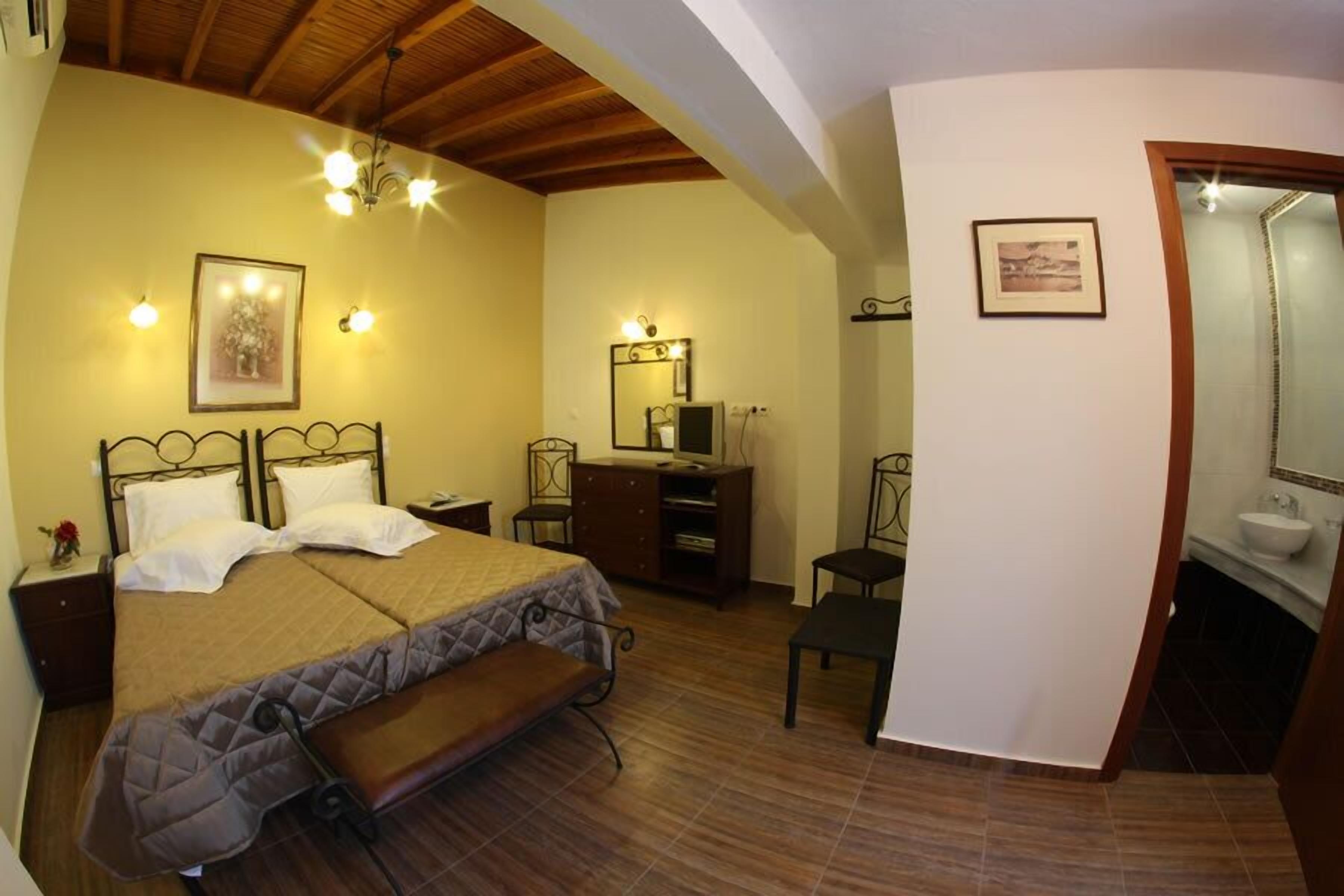 Un dormitorio con cama, mesitas de noche, un banco, cómoda, espejo y baño con lavamanos.