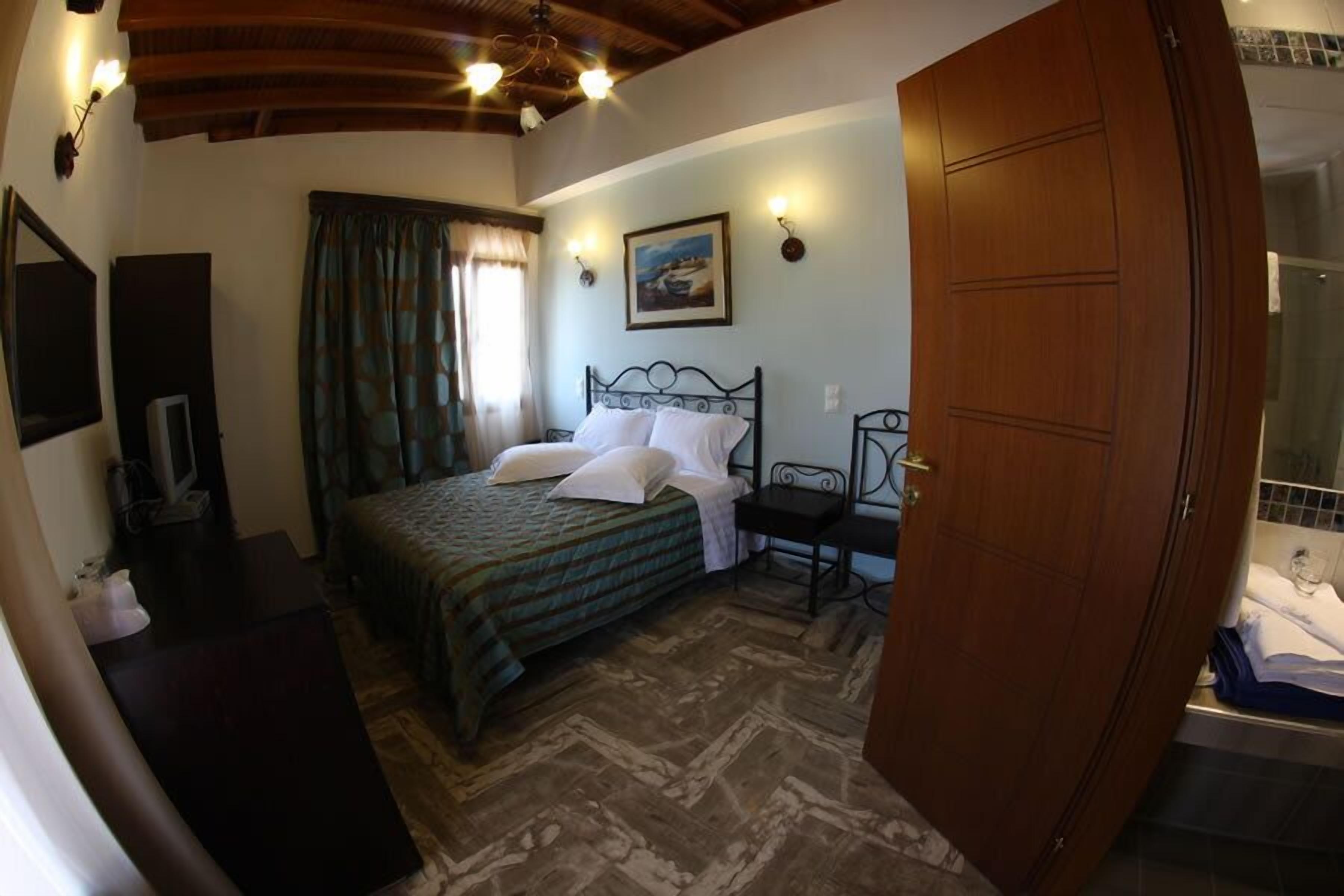 A bedroom with a bed, a wooden wardrobe, a desk, a chair, and a bathroom visible through an open door.