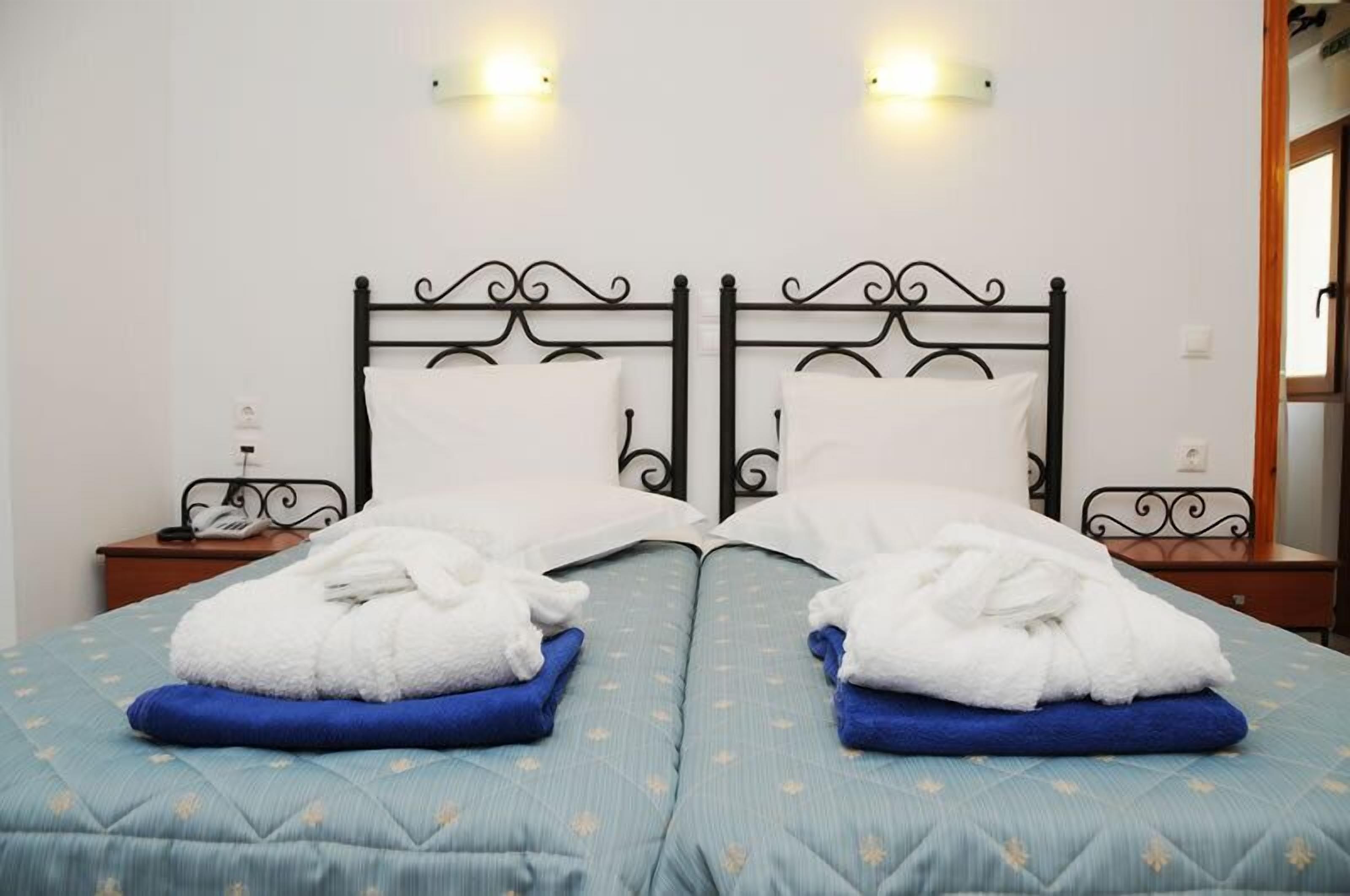 A double bed with a blue quilt, two white towels, and a black metal headboard.