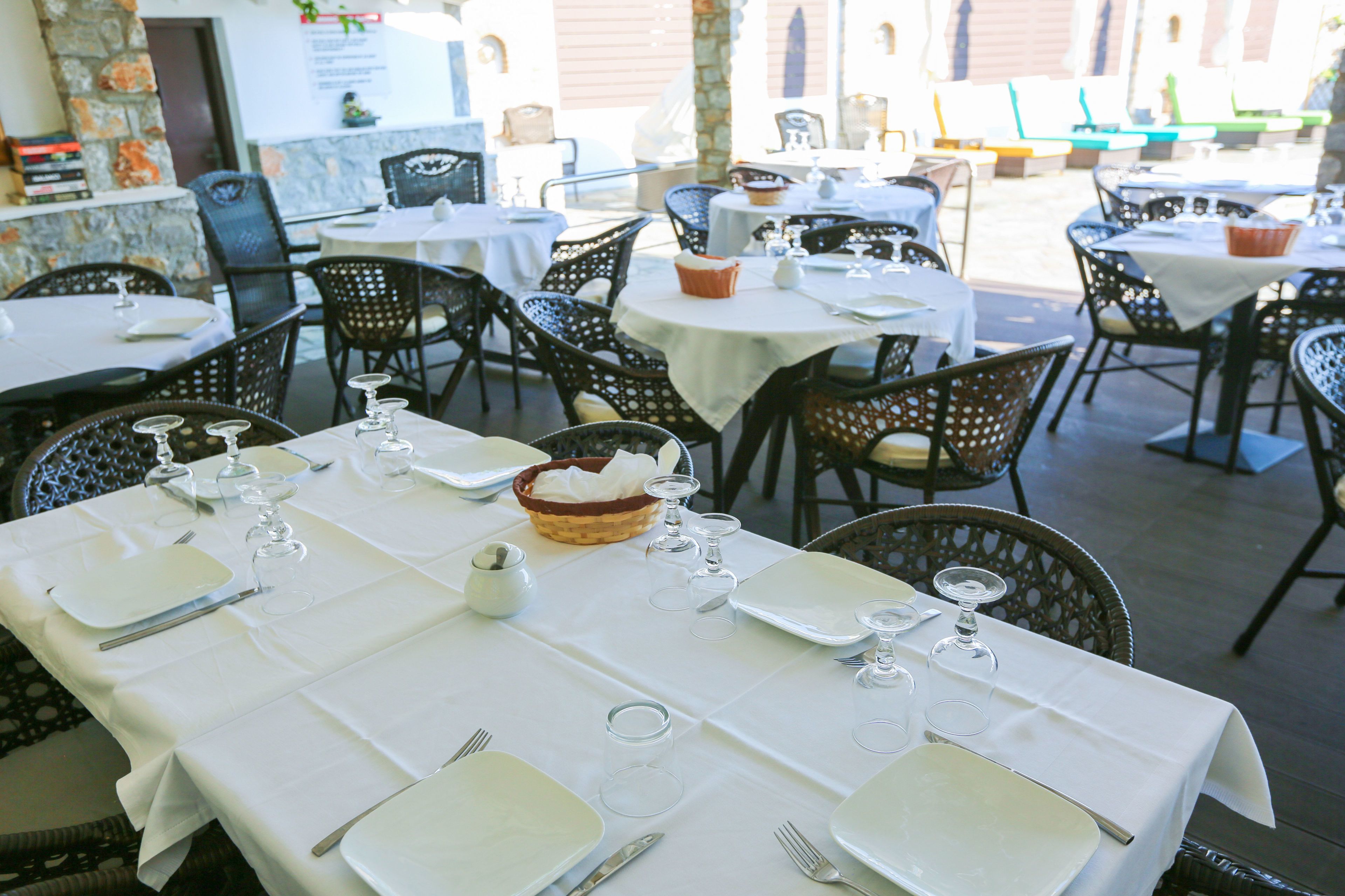 A restaurant with outdoor seating, white tablecloths, and wicker chairs.