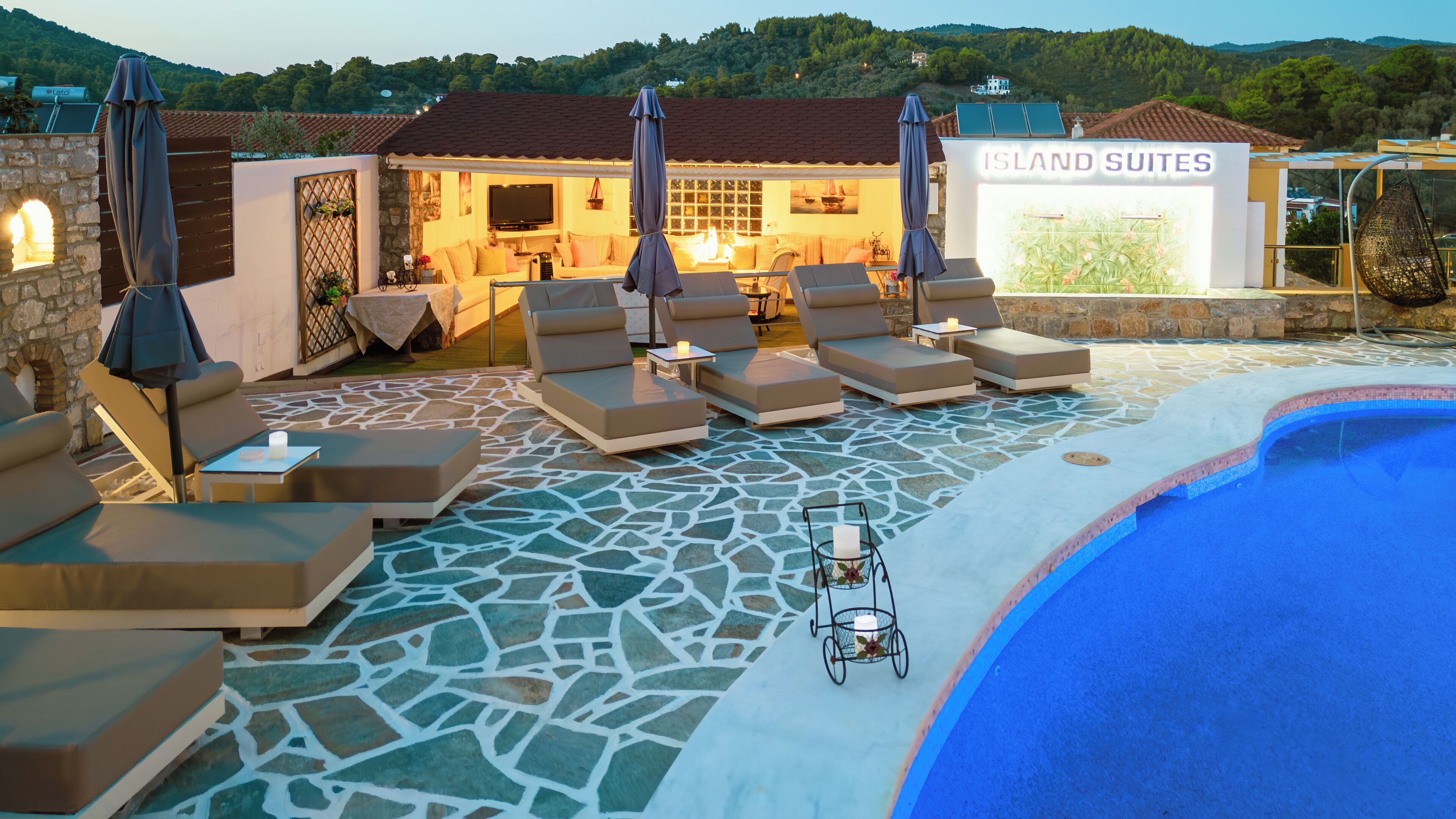 A pool area with lounge chairs, a stone-tiled floor, and a sign reading "ISLAND SUITES".