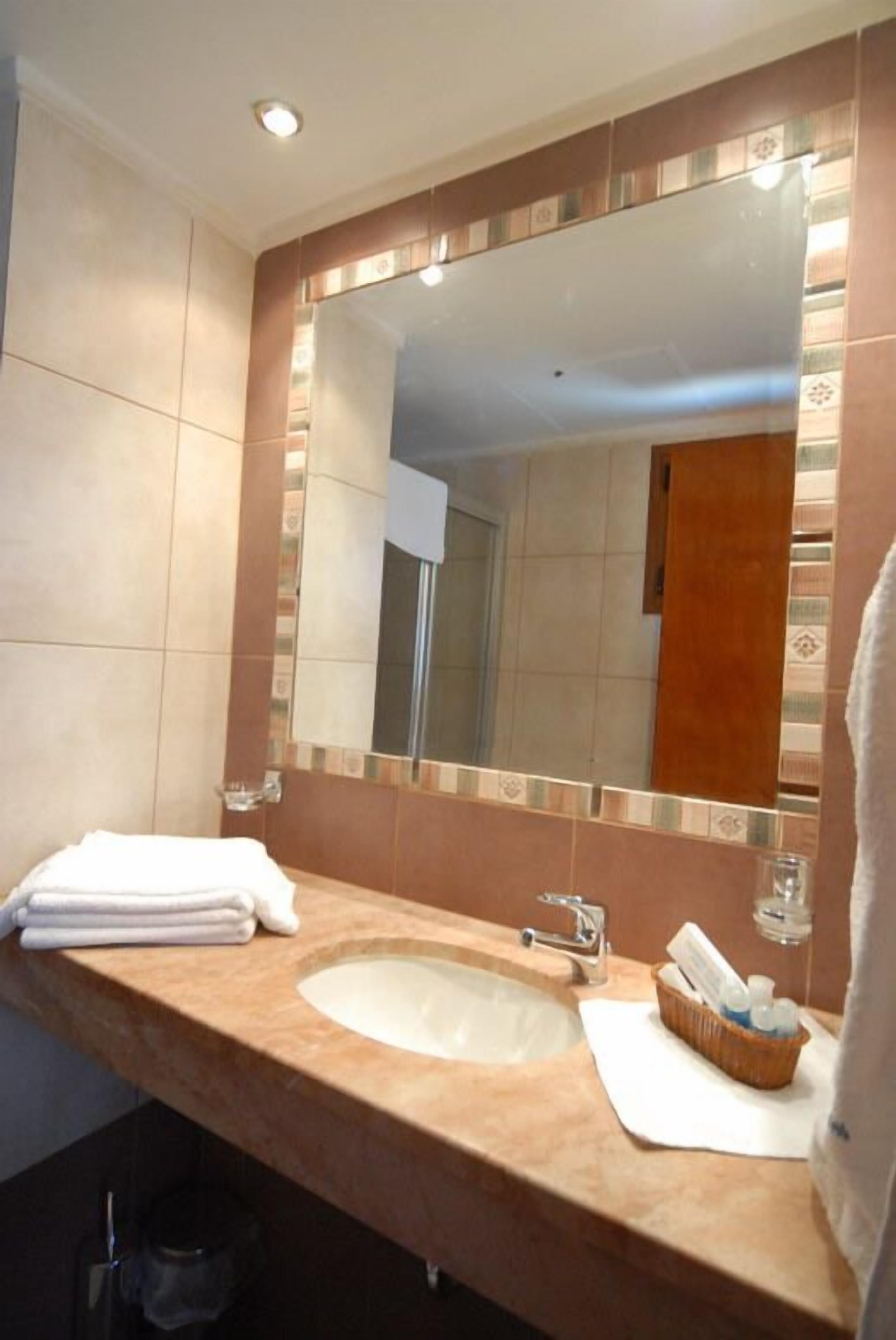 A bathroom with a beige sink, a large mirror, and a towel rack.