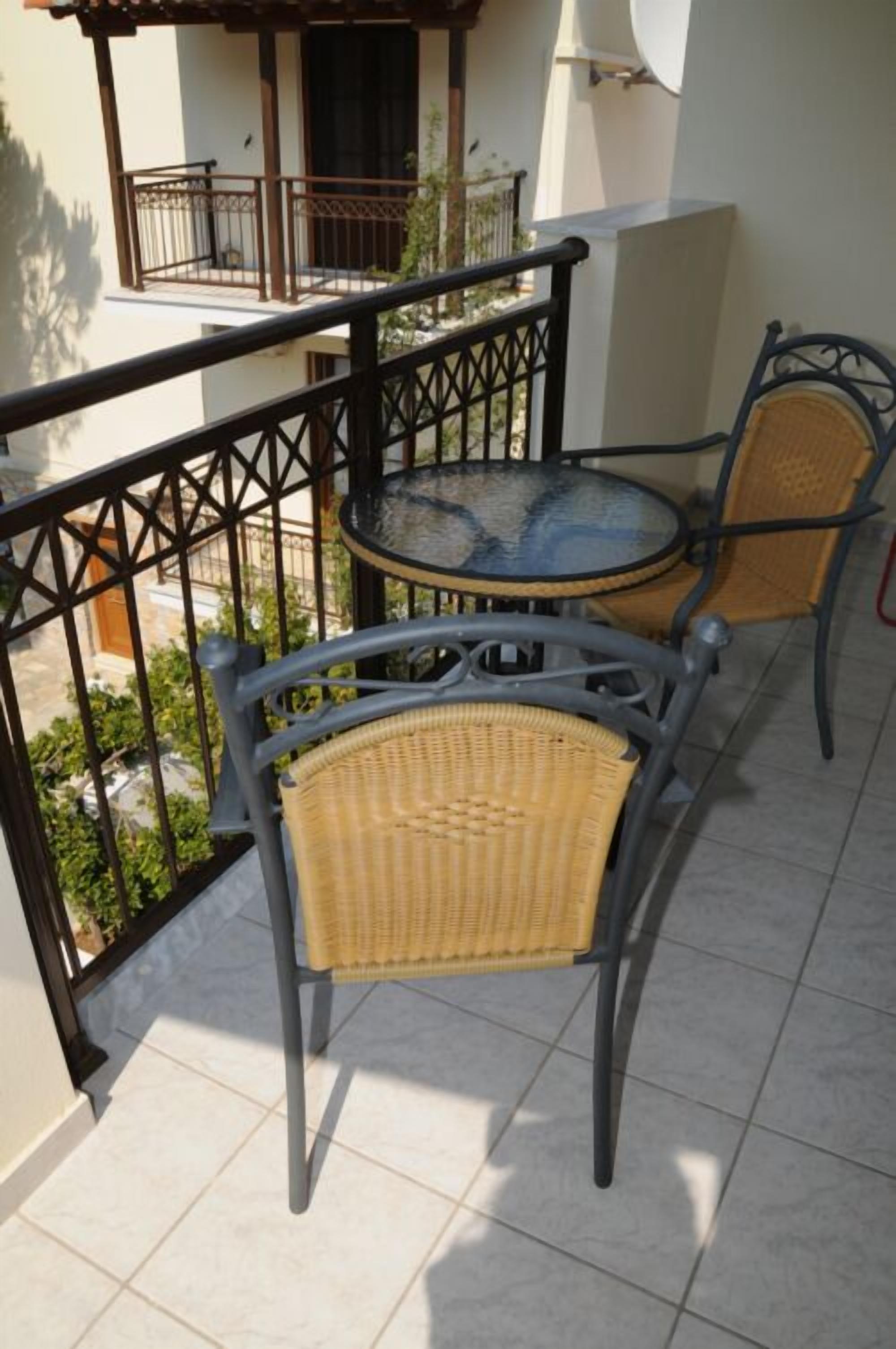 Een balkon met twee rieten stoelen en een kleine ronde tafel, voorzien van een metalen leuning en uitzicht op de omgeving.