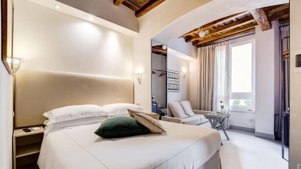 Un dormitorio con una cama grande, una silla, una mesita y una ventana con cortinas.