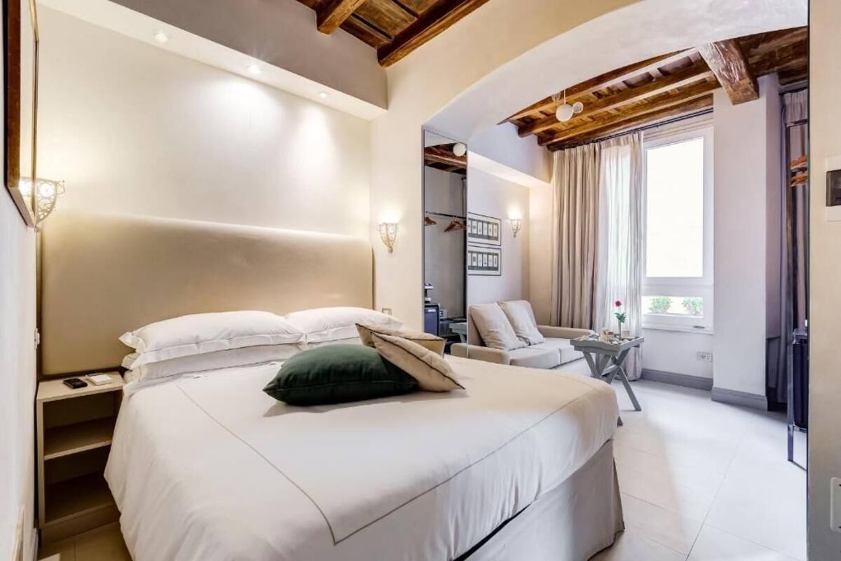 A bedroom with a large bed, a chair, a small table, and a window with curtains.