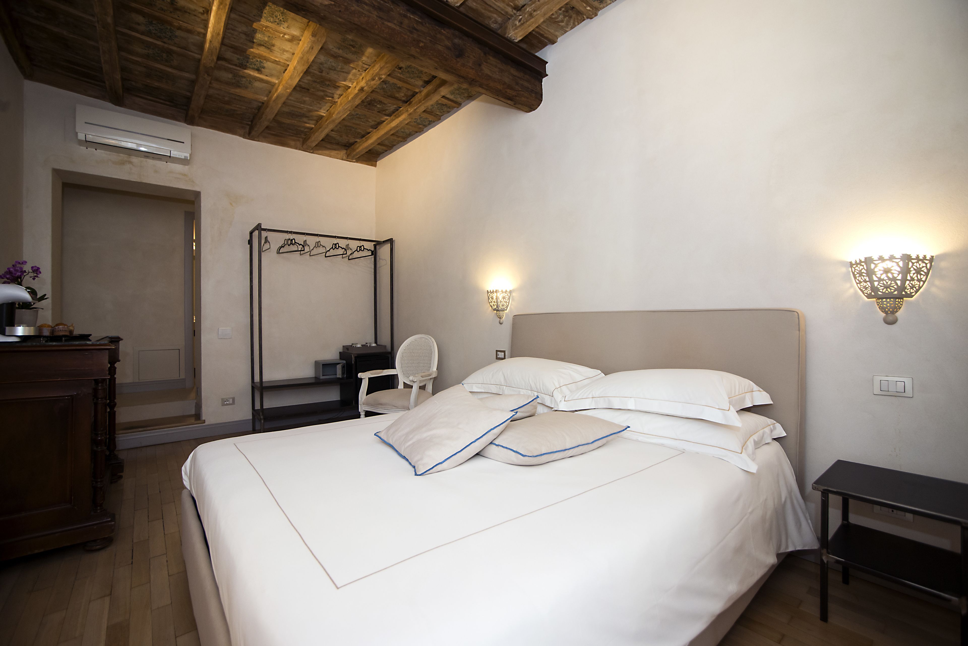 A bedroom with a large bed, a wooden ceiling, a desk, a chair, and wall-mounted lights.