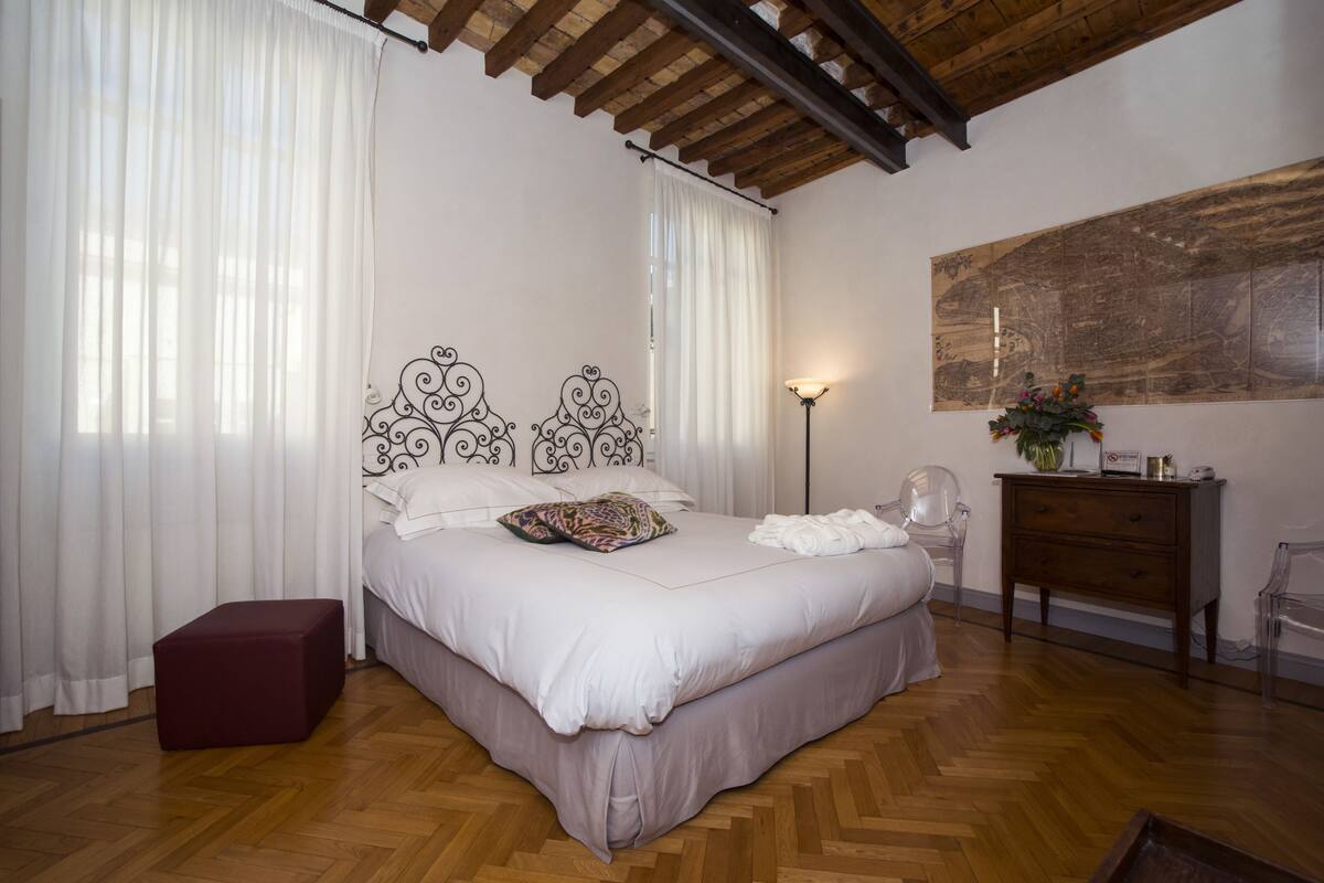 A bedroom with a bed, curtains, a lamp, a dresser, and a map on the wall.