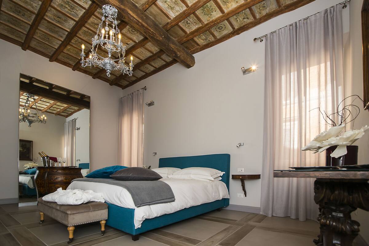 A bedroom with a large bed, a dresser, a mirror, and a chandelier.
