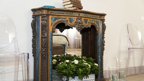 Espejo antiguo ornamentado con un arreglo floral en primer plano, flanqueado por sillas de plástico transparente.