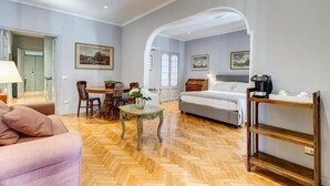 Una habitación amplia con suelo de madera en patrón de espiga, una cama, un sofá, una mesa de comedor con sillas y una cafetera.