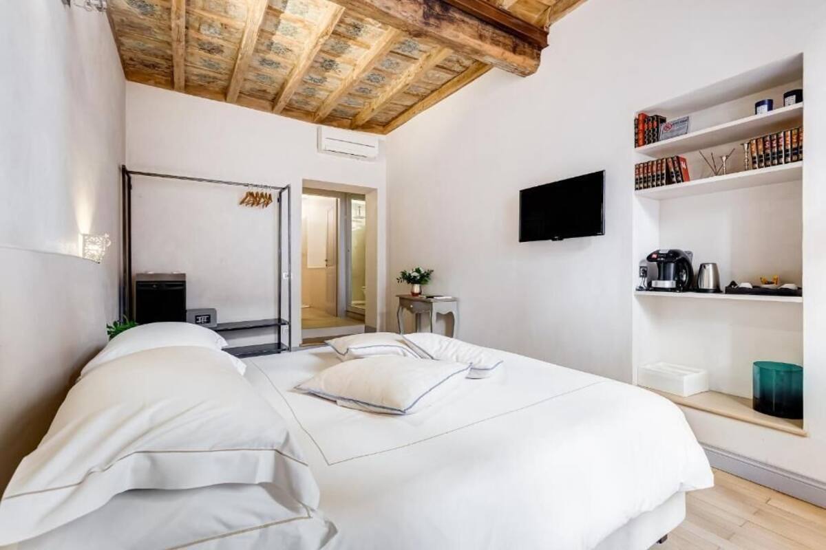 A modern hotel room with a large bed, a TV mounted on the wall, and a bookshelf with books and decorative items.