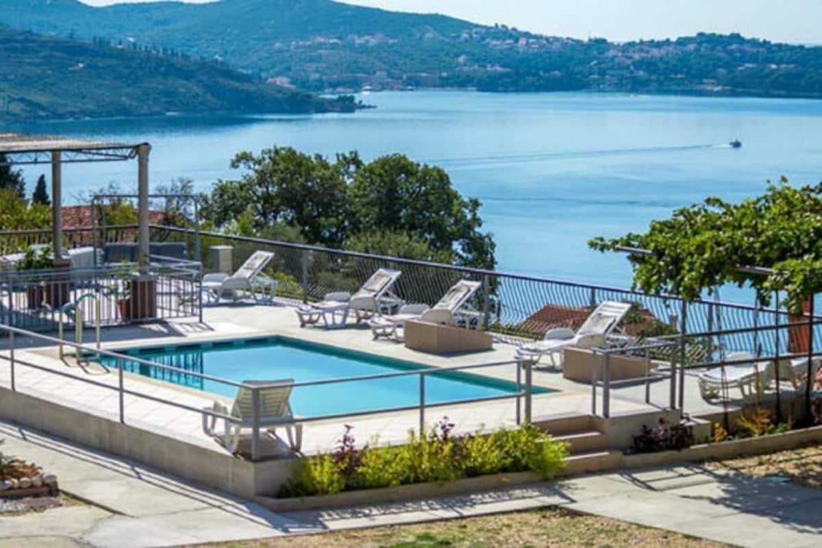 A pool area with lounge chairs and a pergola overlooking a lake.