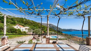 A terrace with a pergola, outdoor seating, and a view of a mountainous landscape and a body of water. - Apartments Klis (Zupa dubrovacka)