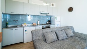 A compact kitchen with white cabinets, a grey sofa, and a coffee machine. - Apartments Klis (Zupa dubrovacka)