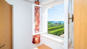 A room with a large window, a wooden door, and a view of a landscaped garden. - Apartments Klis (Zupa dubrovacka)