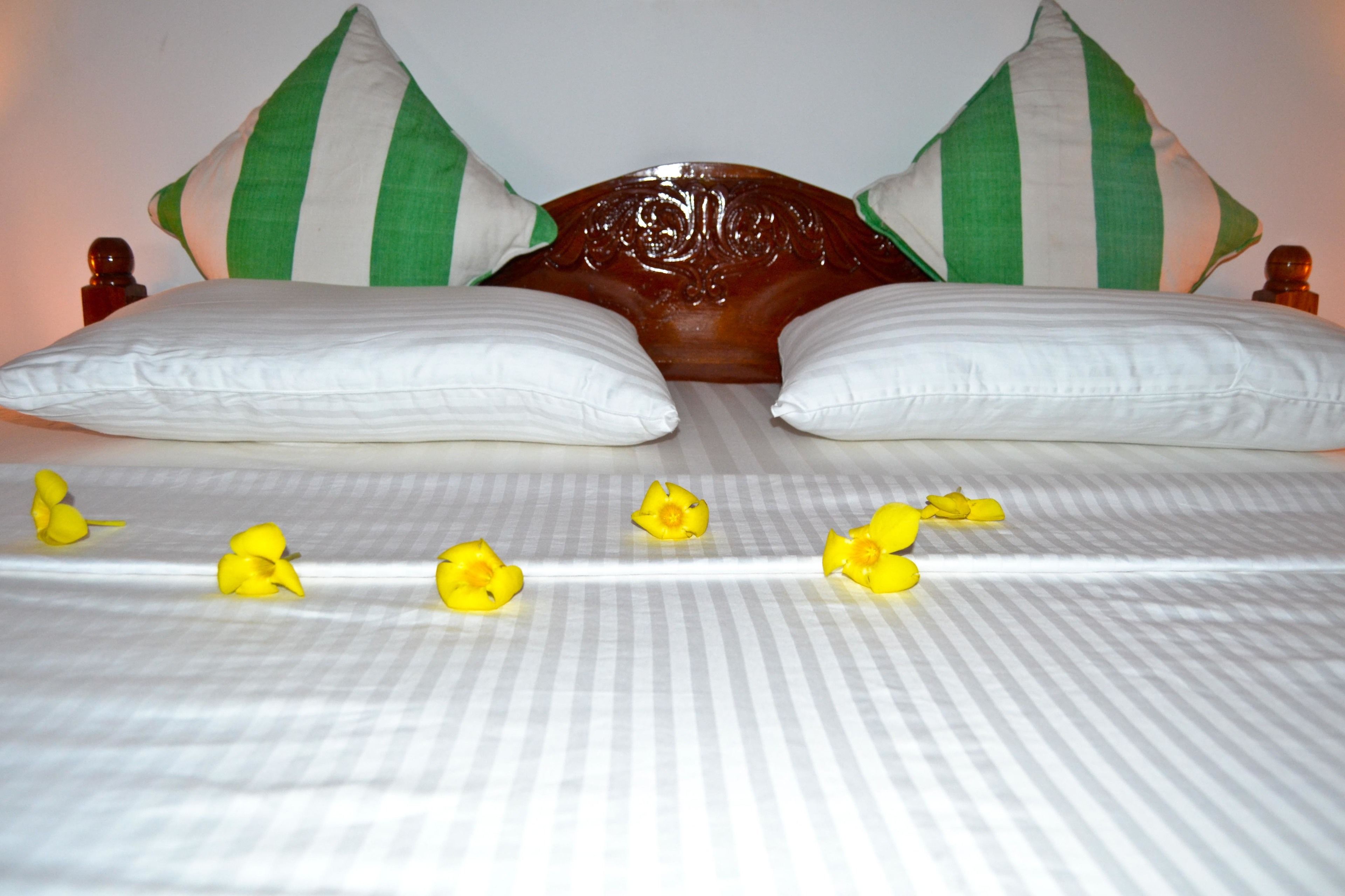 A bed with white pillows and a wooden headboard, adorned with green and white striped pillows.