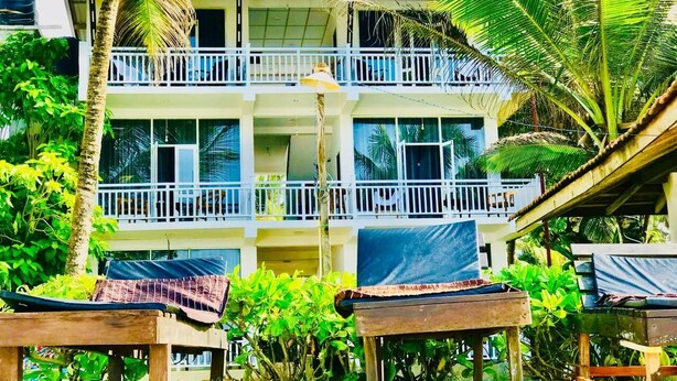 A multi-story building with balconies, surrounded by lush greenery and palm trees. - Ocean Breeze Villa (Boossa)