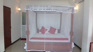 A four-poster bed with a canopy, two pillows, and a red bedspread in a room with white walls and a wooden door. - Ocean Breeze Villa (Boossa)