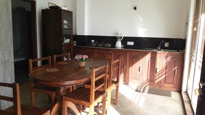 A compact kitchen with wooden cabinets, a dining table with chairs, and a small countertop with a blender. - Ocean Breeze Villa (Boossa)