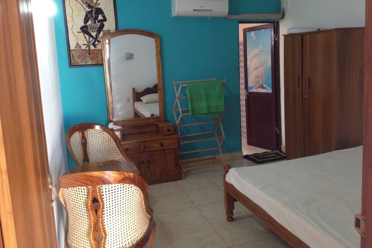 A bedroom with a bed, a wooden dresser, a chair, a mirror, and a painting on the wall.