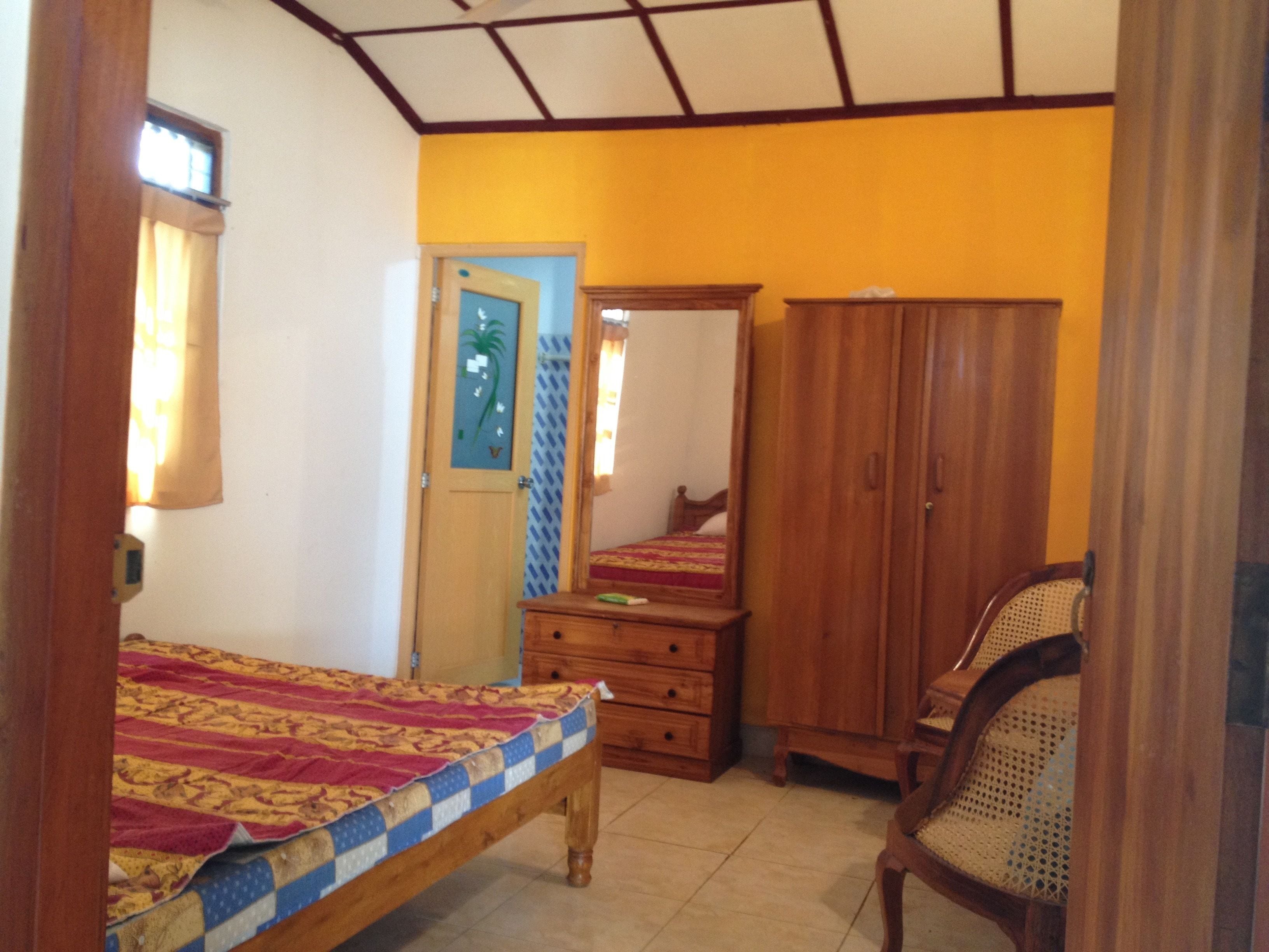 Un dormitorio con una cama, un armario de madera, una silla y una puerta con espejo.